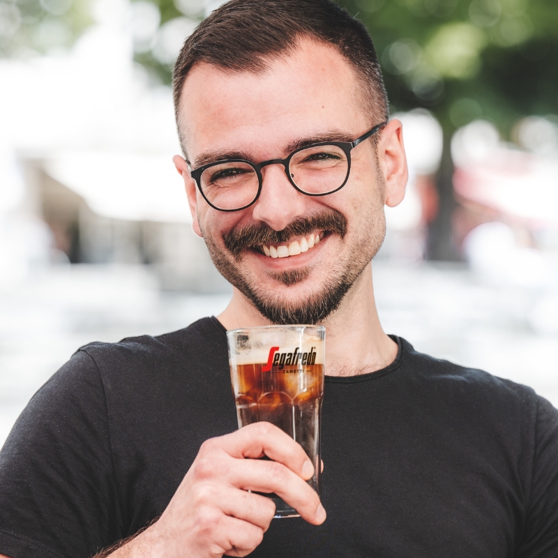 Mann hält ein Glas mit Iced Americano Kaffee